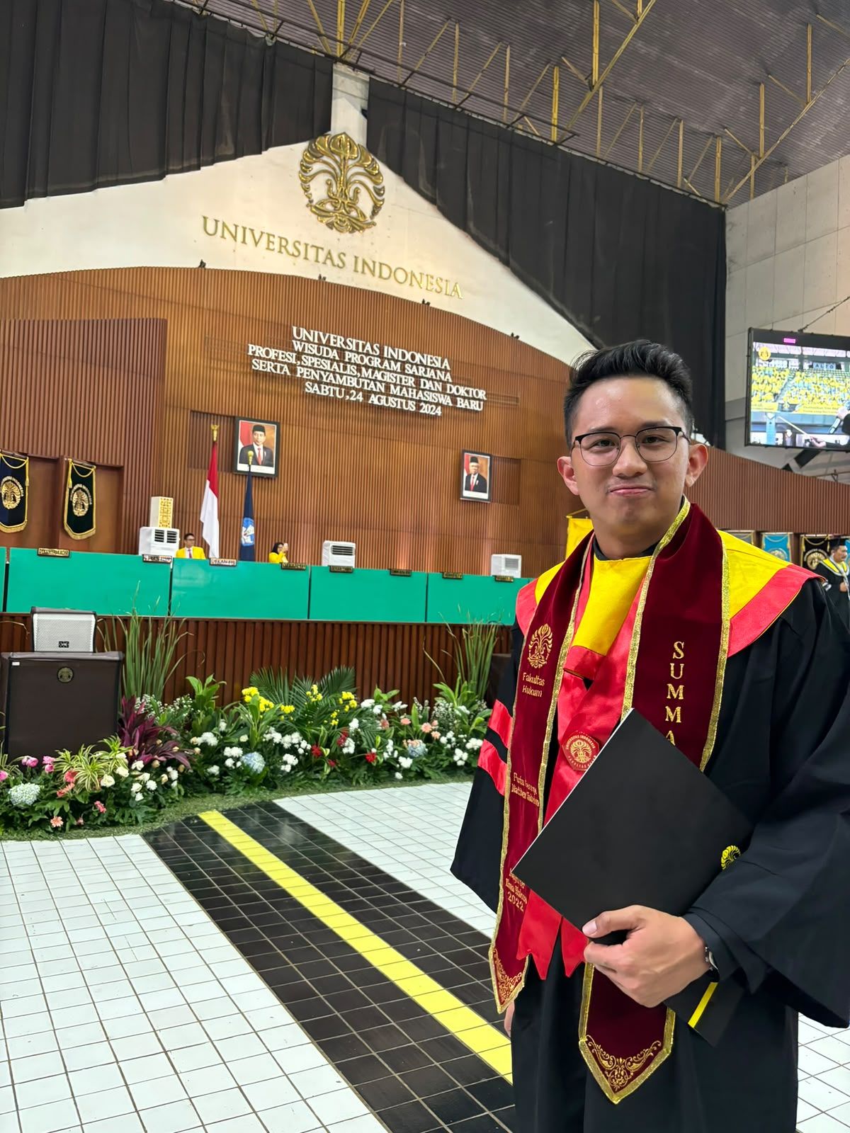 Dr. (Cand.) Putu George Matthew Simbolon, S.H., M.H. at Universitas Indonesia graduation, wearing a Summa Cum Laude sash