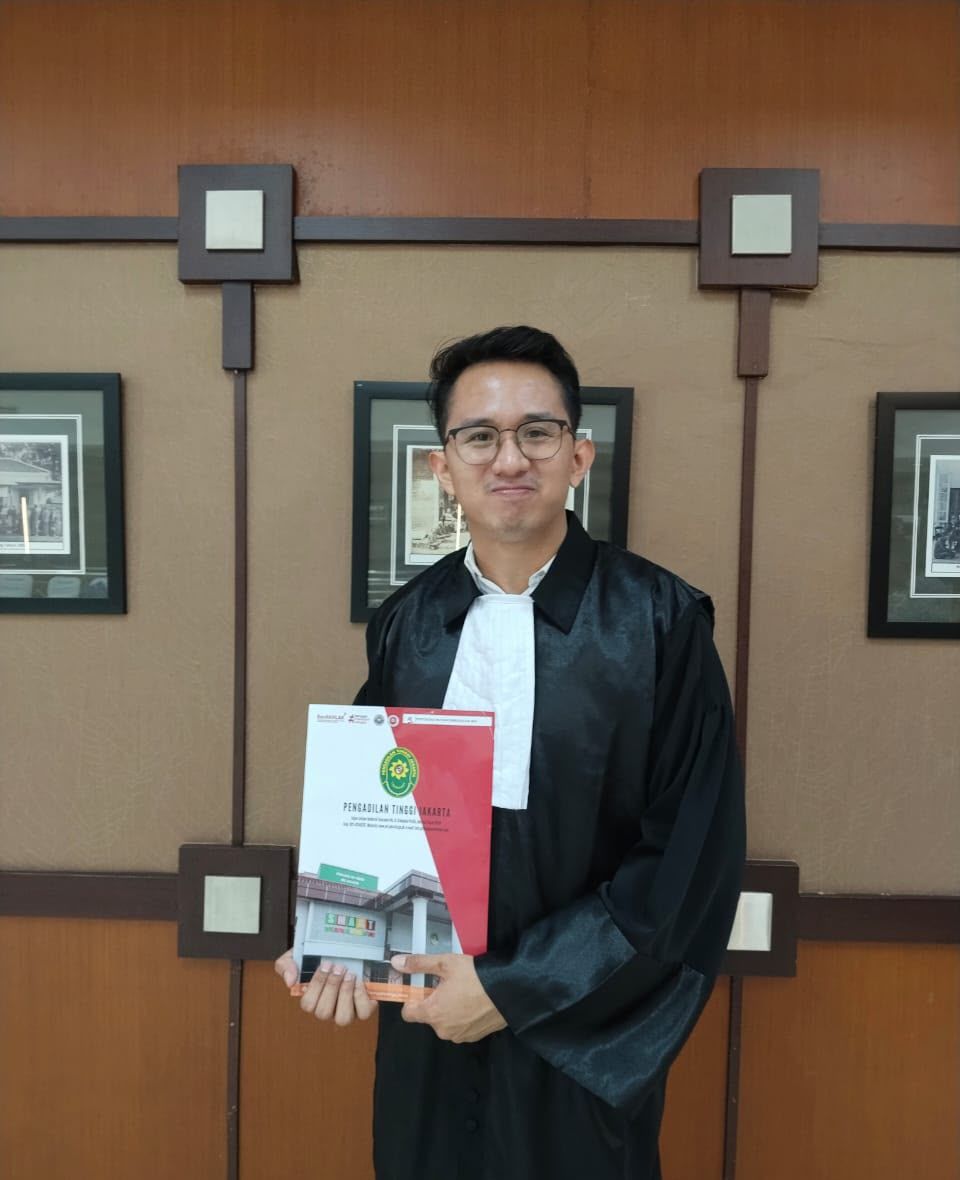 Dr. (Cand.) Putu George Matthew Simbolon, S.H., M.H. in advocate robes at the Jakarta High Court, holding a court folder
