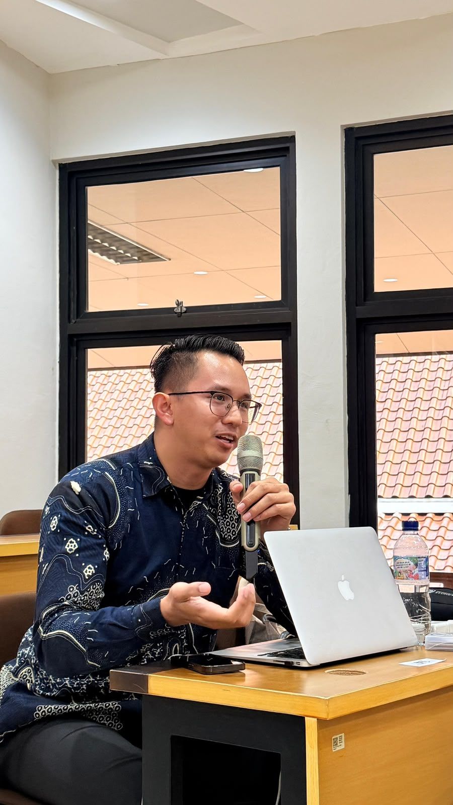 Dr. (Cand.) Putu George Matthew Simbolon, S.H., M.H. speaking with a microphone at a seminar