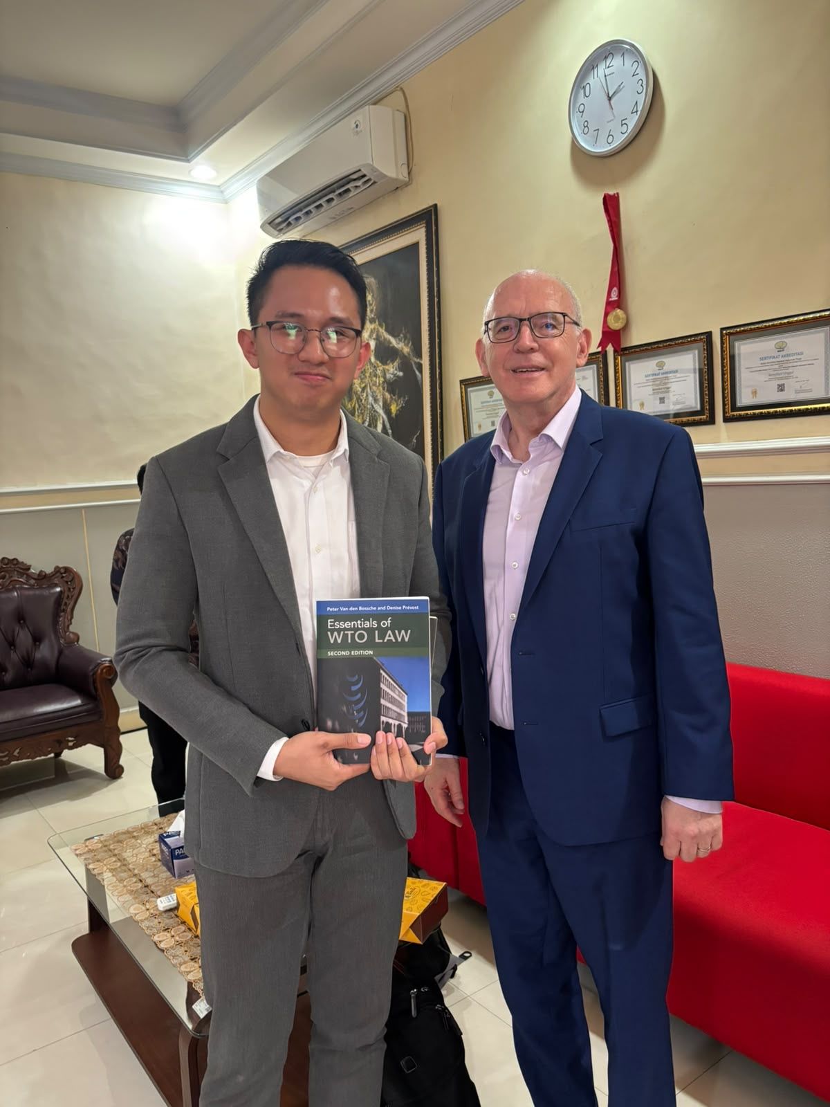 Dr. (Cand.) Putu George Matthew Simbolon, S.H., M.H. holding a copy of Essentials of WTO Law
